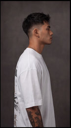 Ouffits white mythic warrior graphic oversized t-shirt — Creator & Destroyer – Man wearing a white t-shirt with black text and graphics from side angle, against a brown background