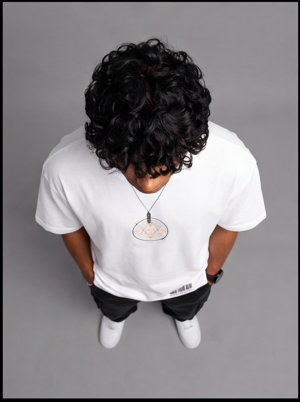 Ouffits white mythic warrior graphic oversized t-shirt — Creator & Destroyer – A person viewed from above wearing a white long-sleeve T-shirt with a small circular chest graphic, black pants, and white sneakers against a plain gray studio background.