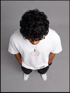 Ouffits white mythic warrior graphic oversized t-shirt — Creator & Destroyer – A person viewed from above wearing a white long-sleeve T-shirt with a small circular chest graphic, black pants, and white sneakers against a plain gray studio background.