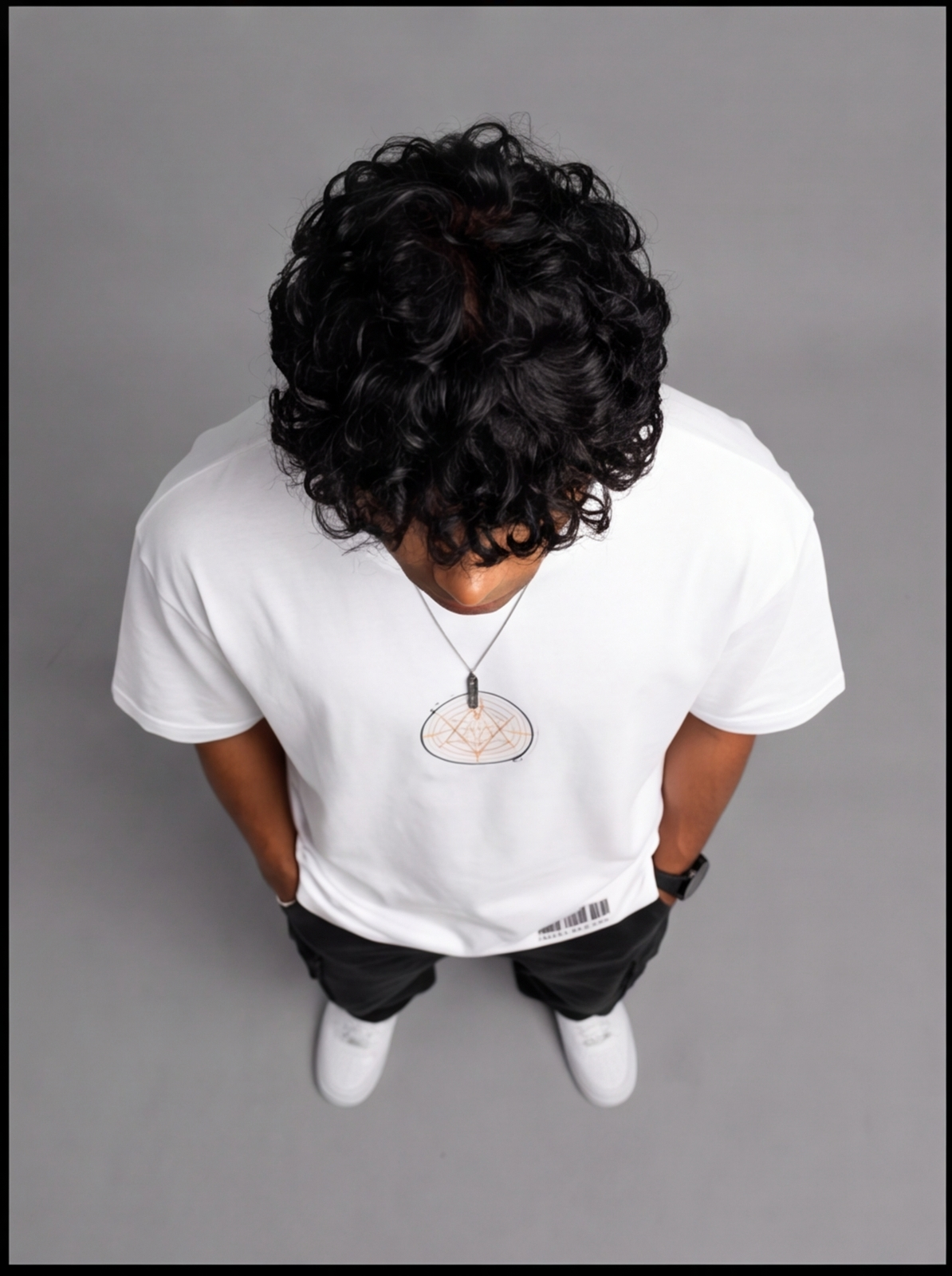 Ouffits white mythic warrior graphic oversized t-shirt — Creator & Destroyer – A person viewed from above wearing a white long-sleeve T-shirt with a small circular chest graphic, black pants, and white sneakers against a plain gray studio background.